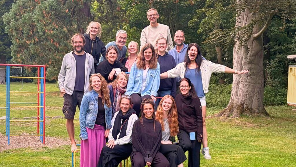 Das Team der Demokratischen Schule Infinita im Herzogtum-Lauenburg steht gemeinsam auf einer Wiese bei einem Spielplatz in Steinhorst.